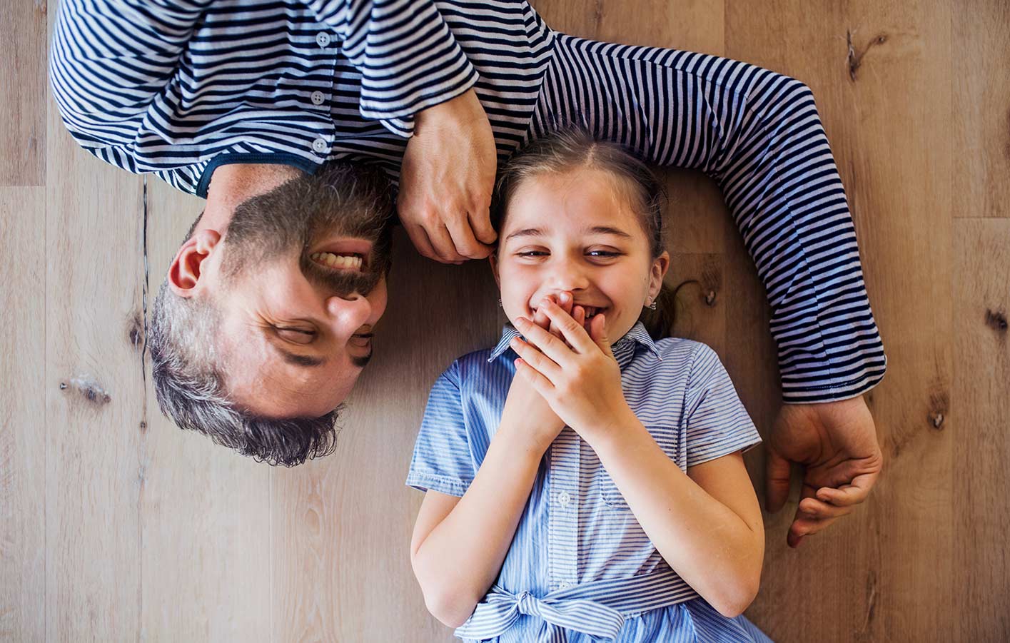 Vater und Tochter auf Parkettboden liegend - lachen